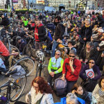 Folla di manifestanti in bici seduti sull'asfalto